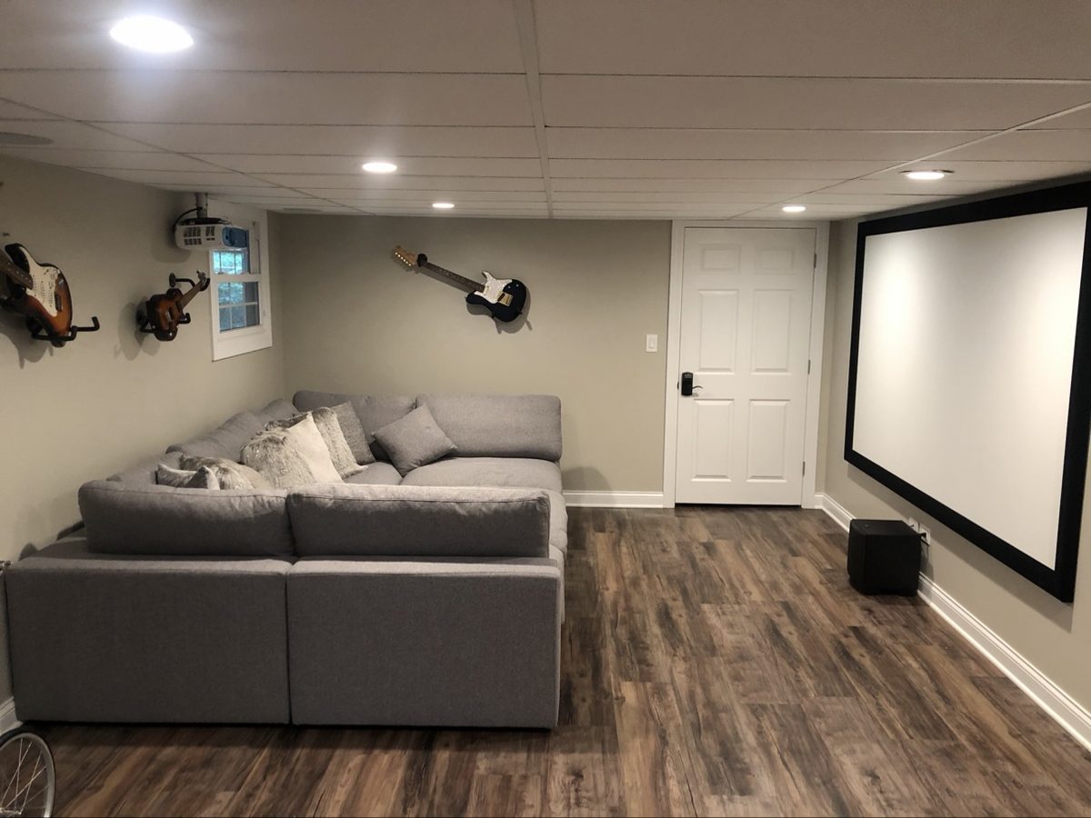 Basement media room with a large projector screen and gray sectional