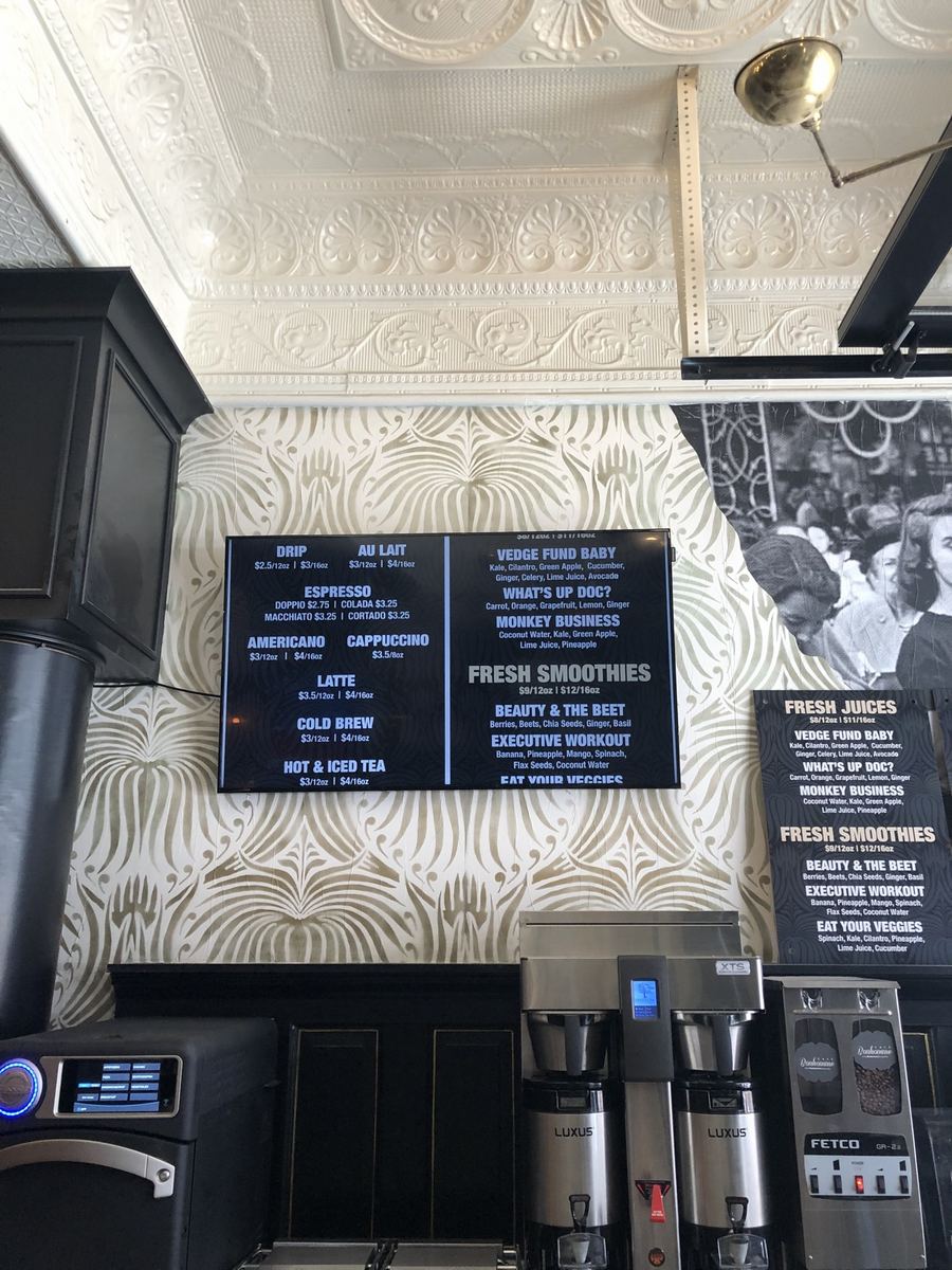 Digital menu board mounted over a coffee bar in a shop