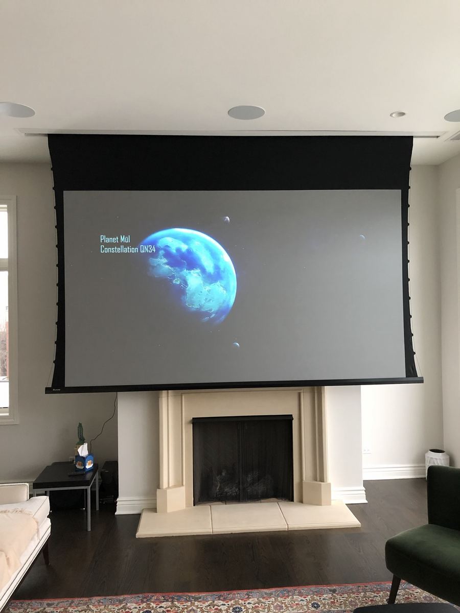 Large motorized projection screen lowered from the ceiling in front of a living room fireplace