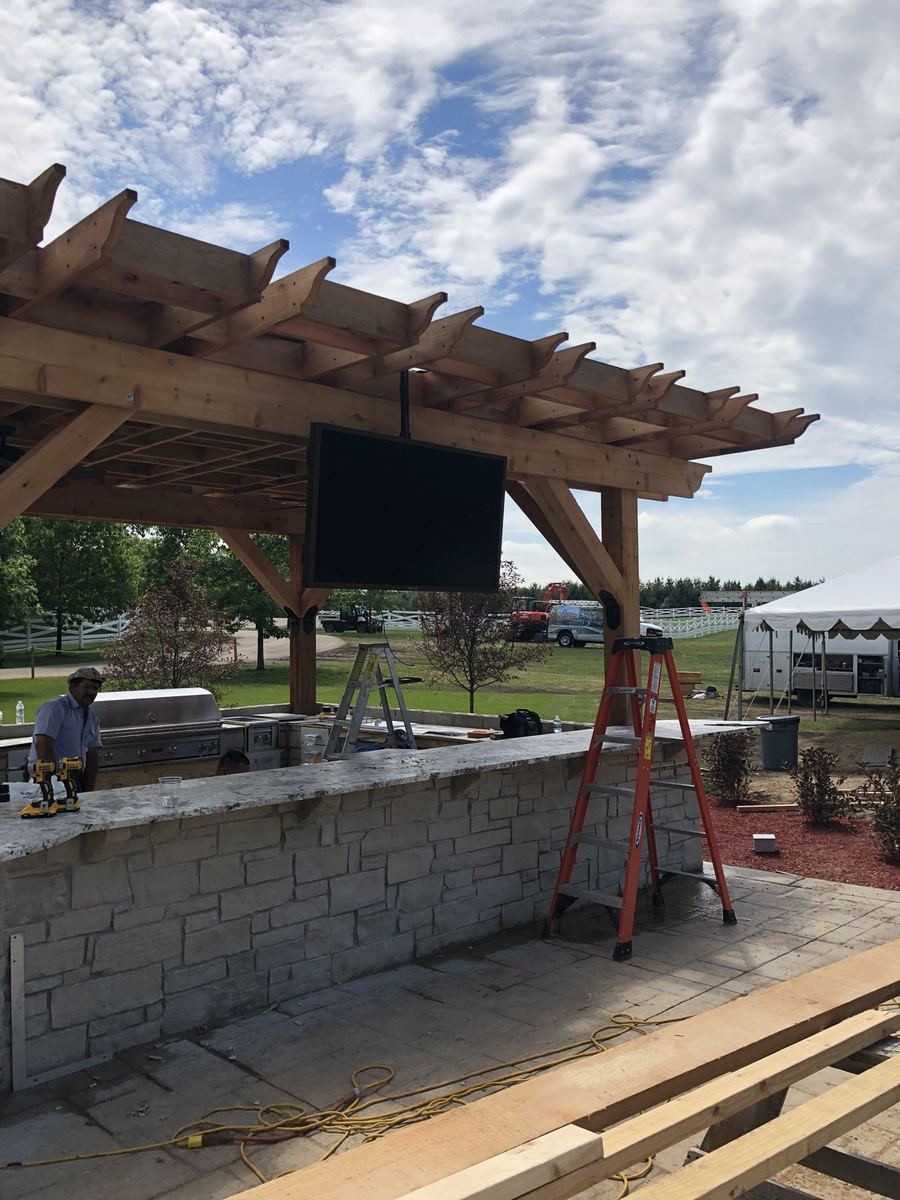 After: front of the TV mounted under the pergola over the outdoor kitchen, pool behind
