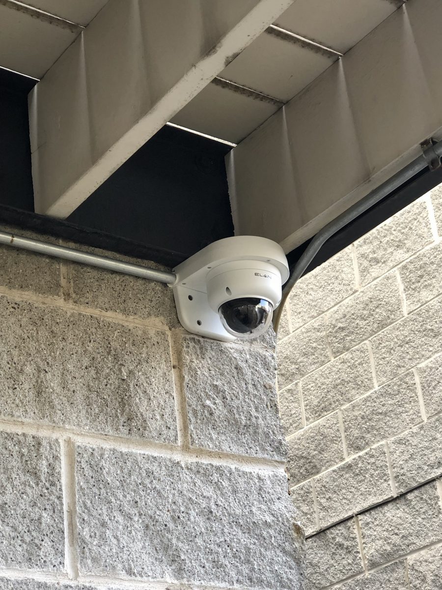 Dome security camera mounted under an exterior soffit on a brick wall