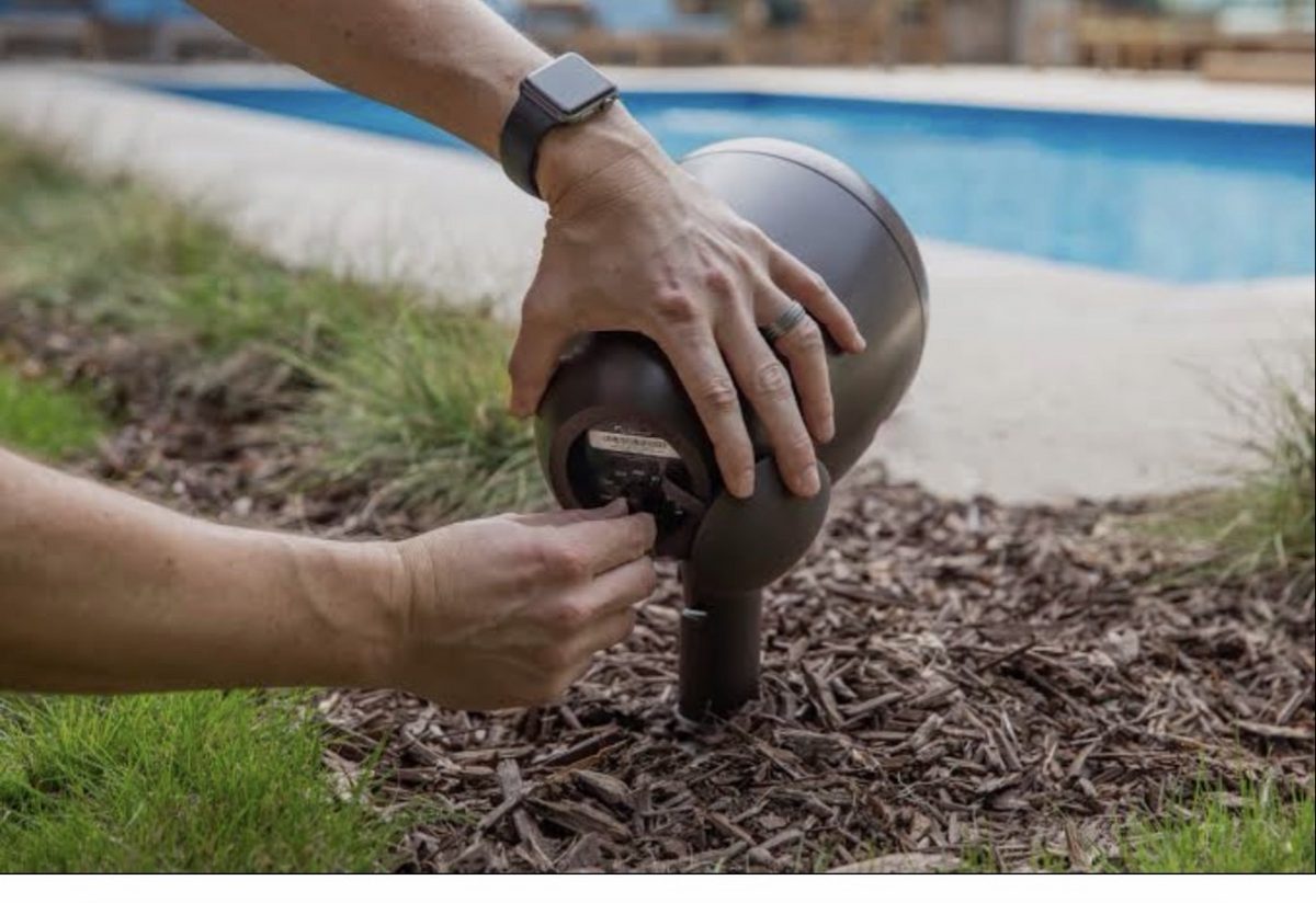 Spike-mounted outdoor speaker being installed in a garden bed by the pool